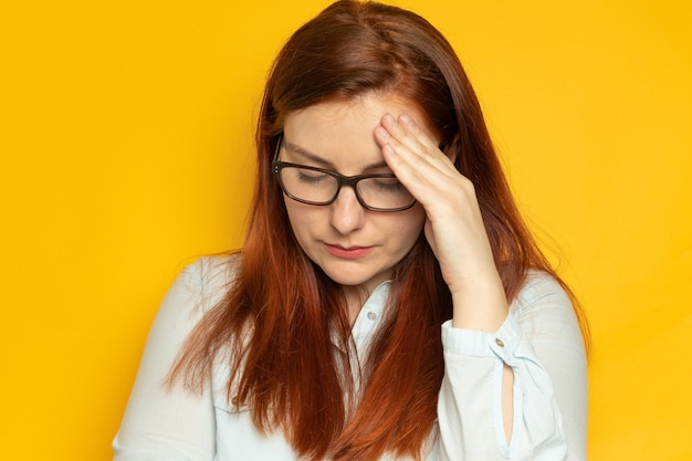 La giovane donna infelice con i capelli lunghi rossi e gli occhiali soffre di mal di testa