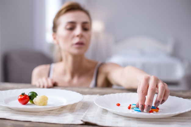 건강에 해로운 중독. 슬픈 쾌활한 여자가 복용하는 약이있는 접시의 선택적 초점