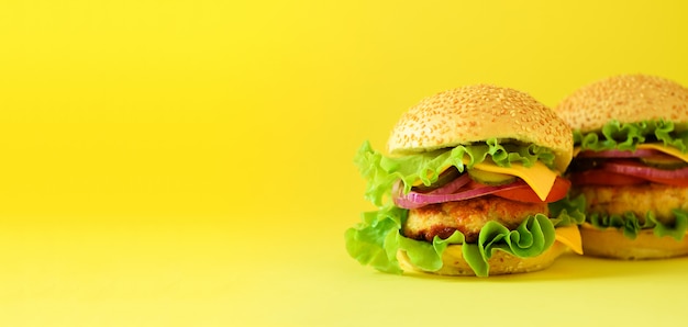 Unhealthy burgers with beef, cheese, lettuce, onion, tomatoes on yellow background. Take away meal. Unhealthy diet concept. 