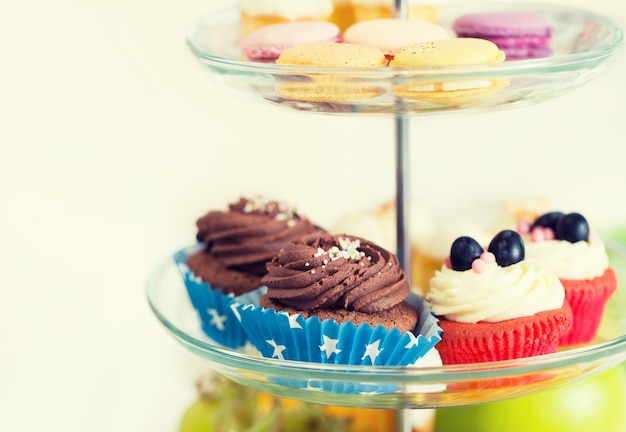 unhealthy eating, sweets, dessert, baking and junk food concept - close up of cake stand with cupcakes and cookies