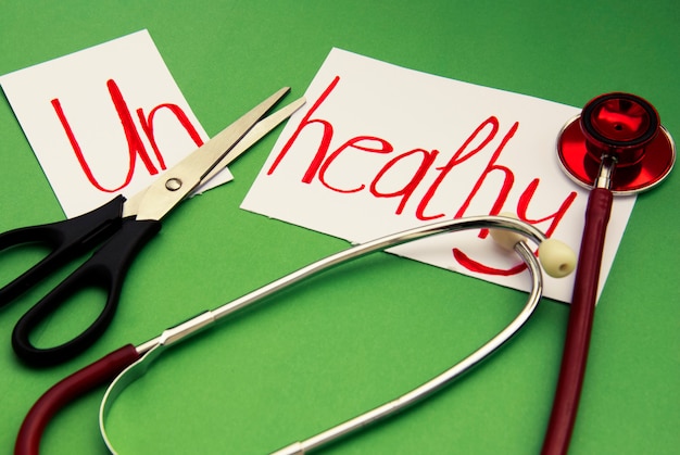 Photo unhealthy inscription. stethoscope and scissors on green . hand writted red inscription. medicine and healthy .