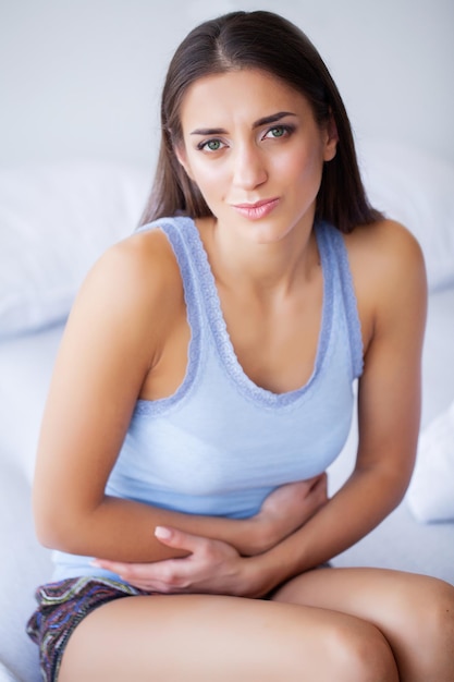 Unhealthy young woman with stomachache leaning on the bed at home