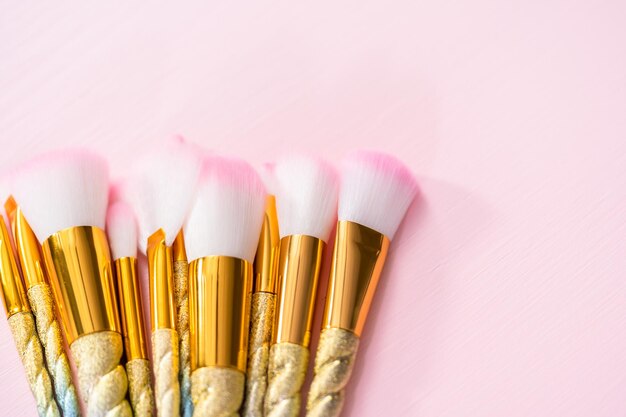 Unicorn color makeup brushes on a pink background.