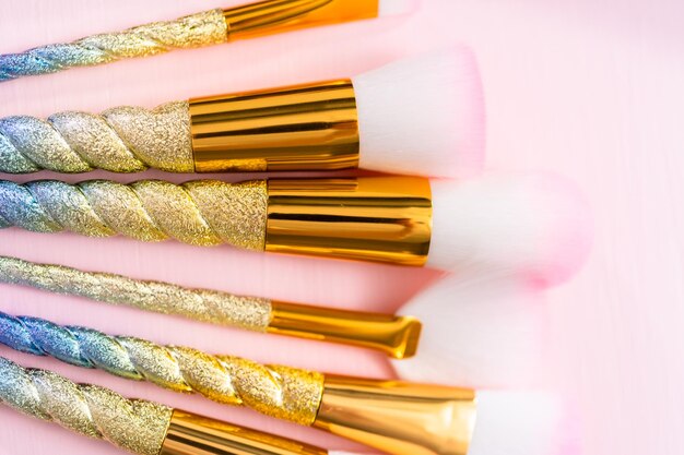 Unicorn color makeup brushes on a pink background.