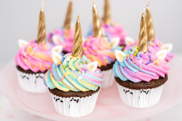 カラフルなバタークリームのアイシングとスプリンクルで飾られたユニコーンカップケーキ。