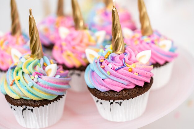 カラフルなバタークリームのアイシングとスプリンクルで飾られたユニコーンカップケーキ。