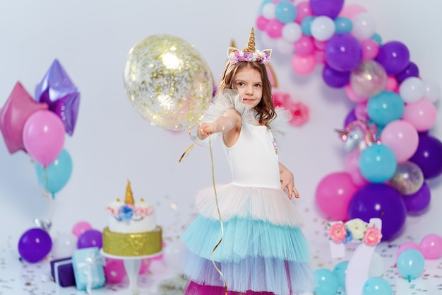 Ragazza dell'unicorno che tiene l'aerostato dei coriandoli dell'oro alla festa di compleanno