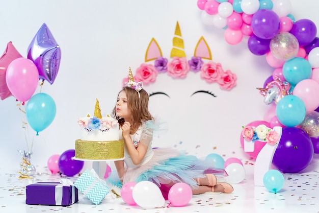 Ragazza dell'unicorno che posa vicino alla torta di buon compleanno