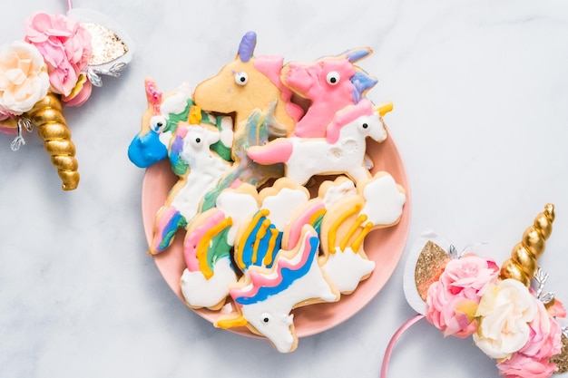 Unicorn shaped sugar cookies decorated by kids with royal icing on pink plate.