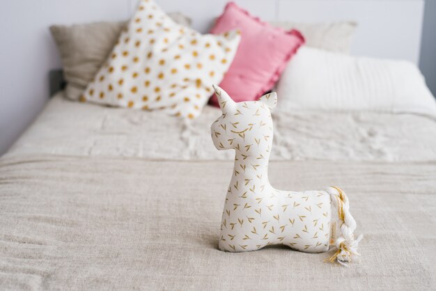 Unicorn soft toy on the bed on the background of multi-colored pillows