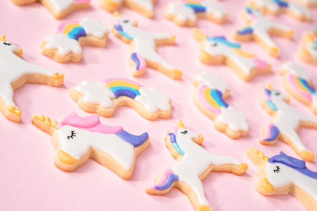 Unicorn sugar cookies decorated with royal icing and food glitter on a pink background.