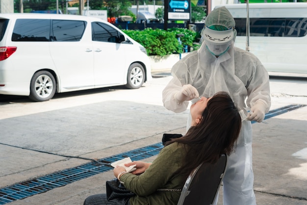 Неизвестный врач в костюме СИЗ и азиатский пациент проверяют образец COVID-19, выполняя мазок из носоглотки или ротоглотки из носа и полости рта в больнице