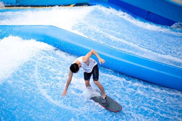 Unidentified man playing surfboard indoor extreme sport.