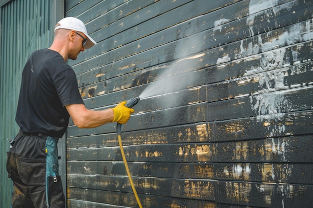 An unidentified man uses a power washer to clean mold and grime off the siding of a house