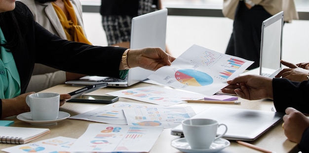 Unidentified unrecognizable businesswoman in casual business clothing holding showing sending company growth target graph chart diagram document paperwork to colleague in meeting room company office.