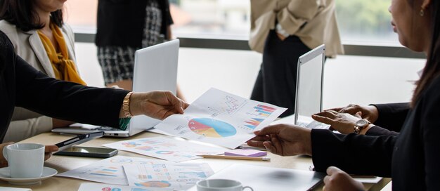 Unidentified unrecognizable businesswoman in casual business clothing holding showing sending company growth target graph chart diagram document paperwork to colleague in meeting room company office.