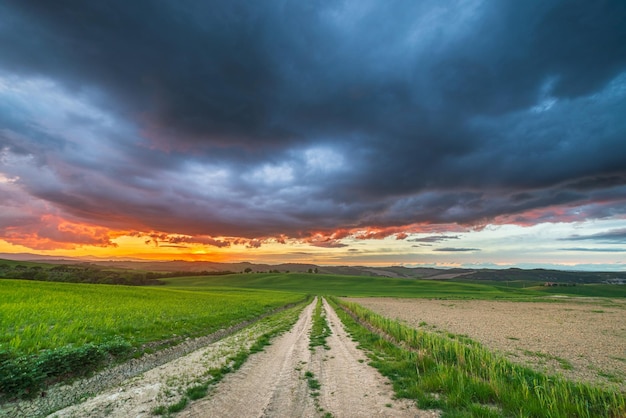 Uniek groen landschap in toscane, italië dramatische zonsonderganghemel, onverharde weg die gecultiveerde heuvels en graanvelden kruist