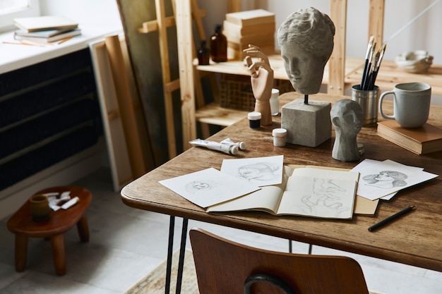 Uniek kunstenaarswerkruimte-interieur met stijlvol bureau, houten ezel, boekenkast, kunstwerken, schilderaccessoires, decoratie en elegante persoonlijke spullen. moderne werkruimte voor kunstenaar.