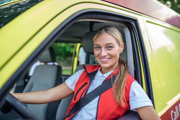 Operatrice di emergenza femminile in uniforme nei primi anni '20 che indossa l'uniforme dei paramedici e guarda fuori dalla finestra aperta dell'ambulanza