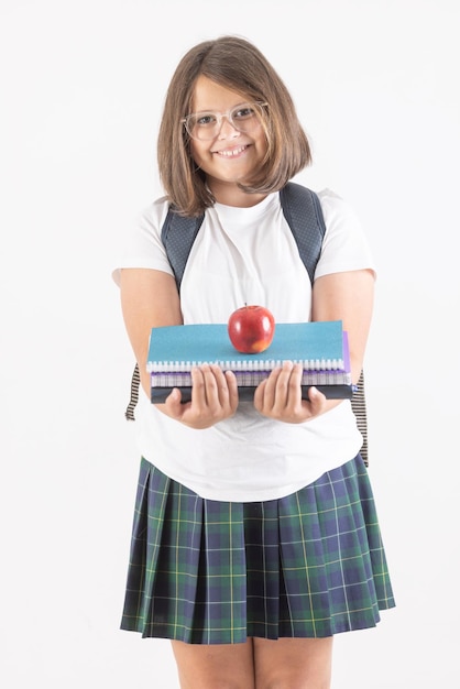 La studentessa in uniforme con gli occhiali e con lo zaino tiene libri e una mela