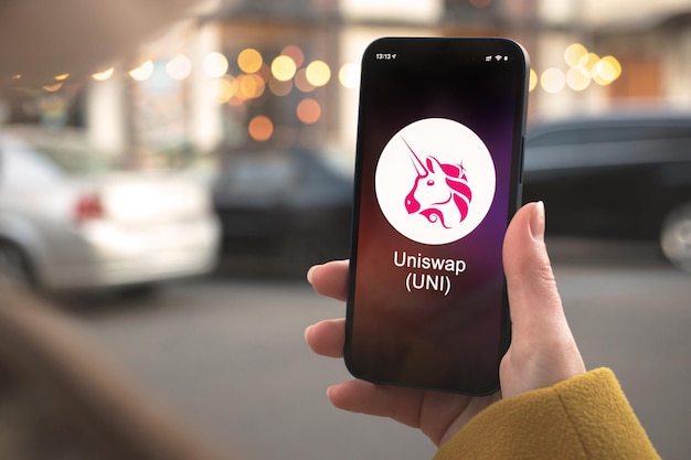 Uniswap uni cryptocurrency-symbool, logo. zakelijk en financieel concept. hand met smartphone, scherm met crypto icoon close-up