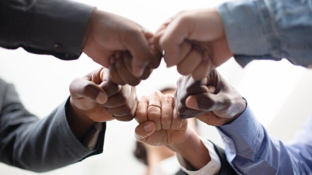 Colleghi uniti in piedi con le mani insieme in un ufficio moderno, celebrando la vittoria, il team building e l'unità