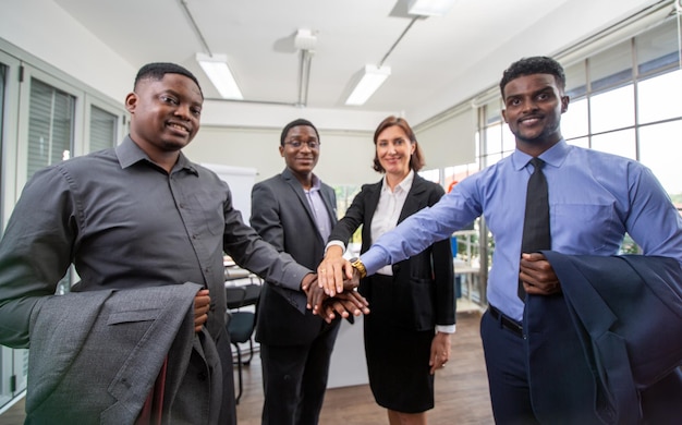 United coworkers standing with their hands together in modern office, celebrating victory, teambuilding and unity