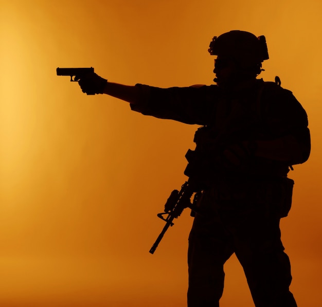 United states Marine Corps special operations command Marsoc raider with weapon aiming pistol. Silhouette of Marine Special Operator orange background