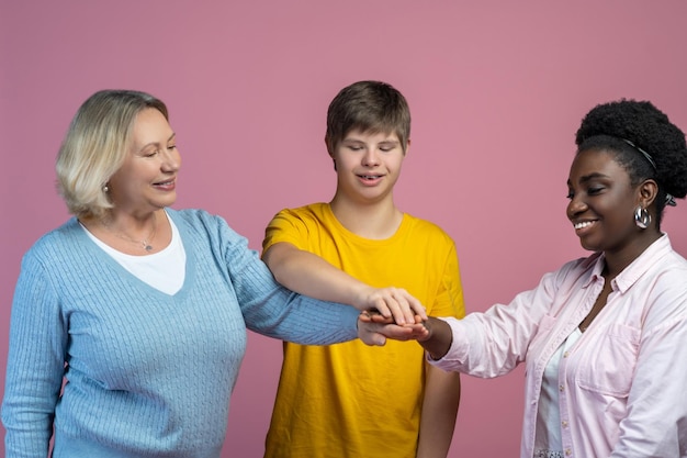 Foto unità. ragazzo sorridente con sindrome di down mamma e donna dalla pelle scura in piedi uno di fronte all'altro che si toccano con le mani tese