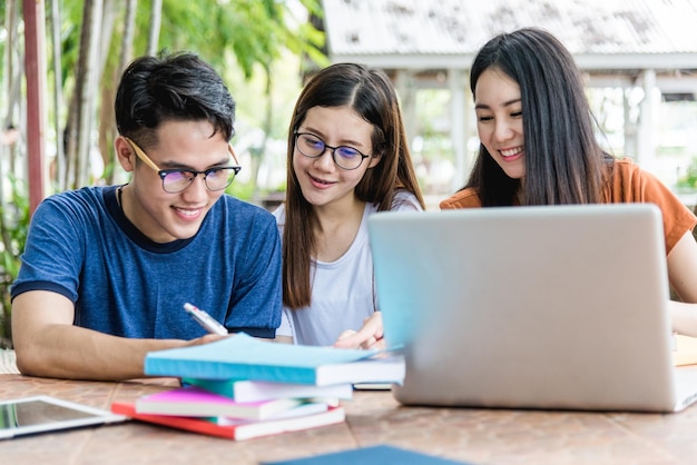 Universiteitsjongeren studenten die samen aan tafel zitten overleggen met boeken, tablet en laptop.