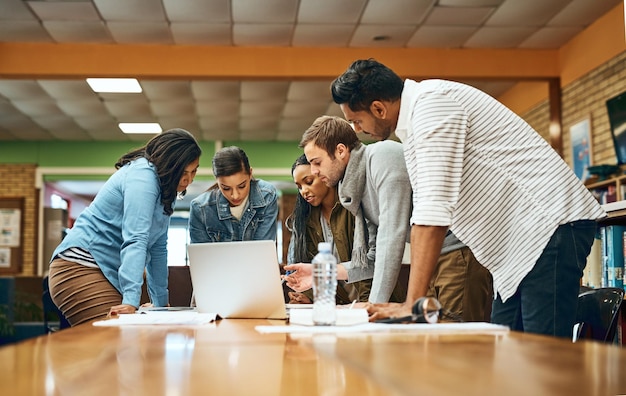 Universiteitsstudent bibliotheek en groepstoewijzing met laptop voor onderzoek teamwerk en samenwerking op de campus Mensen klasgenoten en college leerling met documenten of online voor theorie en aantekeningen