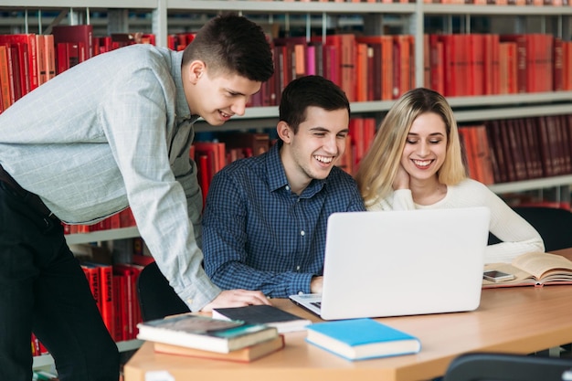 Universiteitsstudenten zitten samen aan tafel met boeken en laptop Gelukkige jonge mensen die groepsstudie doen in bibliotheek