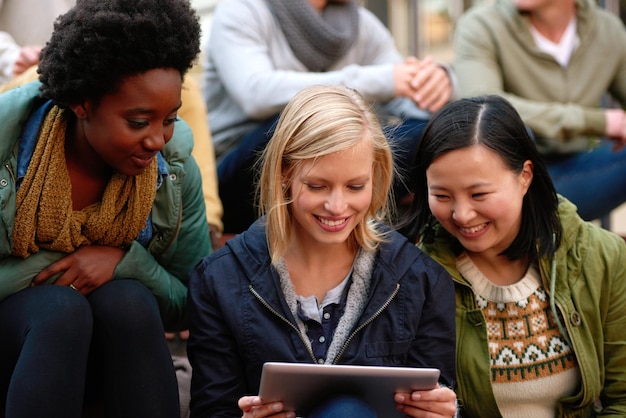 Universiteitsvrienden en glimlachen met tablet buiten voor onderzoek ontspannen of breken op de campus met sociale media College mensen en blij met technologie voor internet streaming of leren en diversiteit