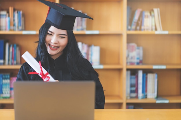 University graduate in graduation gown and mortarboard celebrates in a virtual graduation ceremony