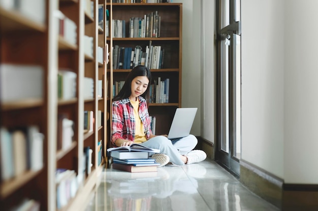 University Library Beautiful smart asian university student uses Laptop Writes Notes for Paper Essay