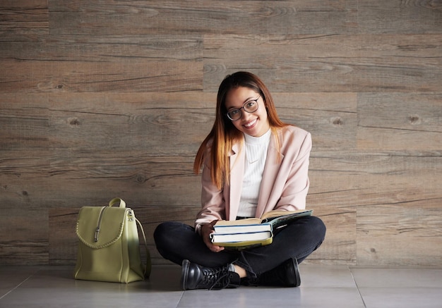 Ritratto universitario di donna felice sul pavimento con libri sullo spazio mockup e istruzione al college conoscenza delle informazioni e studente zaino seduto sullo sfondo del muro con sorriso e libro da studiare