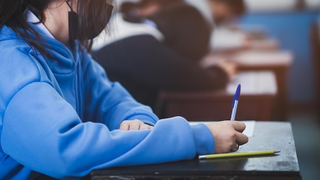 University student holding pen or pencil writing on paper\
answer sheet sitting on chair lecture final exam participates in\
exam room or classroom in uniform student