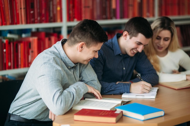 책과 노트북으로 테이블에 함께 앉아 있는 대학생 도서관에서 그룹 공부를 하는 행복한 젊은 사람들