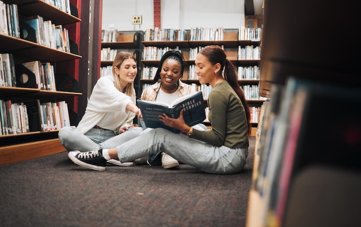Photo university students and women in library with book working on researching and looking up information for group research project college student diversity and friends working on homework together