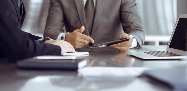 Unknown businessman using tablet computer and working together\
with his colleague while sits at the glass desk in modern office\
teamwork and partnership concept