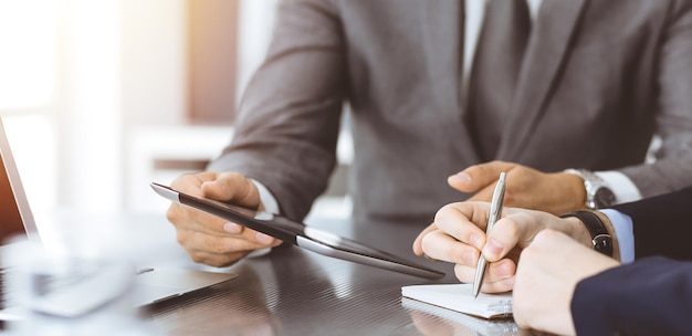 Unknown businessman using tablet computer and working together with his colleague while sits at the glass desk in modern office Teamwork and partnership concept