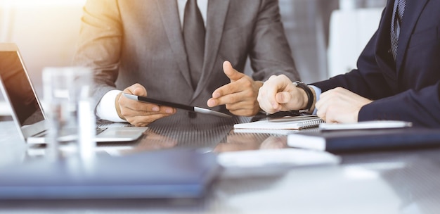 Unknown businessman using tablet computer and working together\
with his colleague while sits at the glass desk in modern office\
teamwork and partnership concept