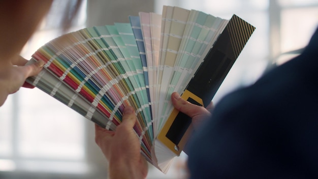 Unknown couple choosing color for walls on swatches book on blurred background