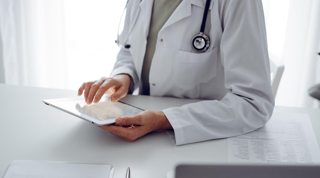 Unknown doctor woman sitting and writing notes at the desk in clinic or hospital office, close up. Medicine concept.