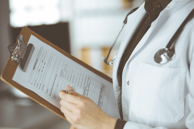 Unknown female doctor using clipboard in clinic. Perfect medical service in hospital.