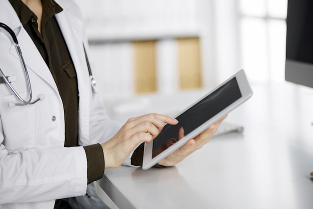 Unknown female doctor using tablet computer in clinic. Perfect medical service in hospital. Medicine concept.