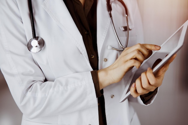 Unknown female doctor using tablet computer in sunny clinic. Perfect medical service in hospital.