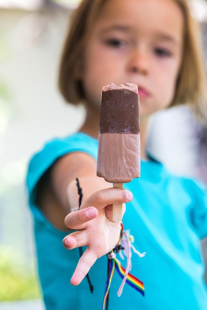 Unknown girl wearing green shirt out of focus holding a milk chocolate ice cream focused on the street in summer Ice cream popsicle eating sweet and summer concept