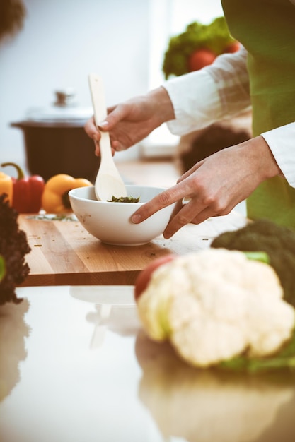 キッチンで調理する未知の人間の手。女性は野菜サラダで忙しい。健康的な食事、そしてベジタリアン料理のコンセプト。