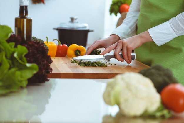 キッチンで調理する未知の人間の手。女性は野菜サラダで忙しい。健康的な食事、そしてベジタリアン料理のコンセプト。